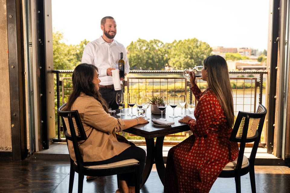 2 women tasting wine and 1 server holding a bottle