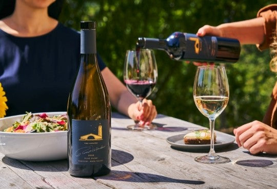 Woman pouring red wine into a glass with another bottle of white wine in the foreground