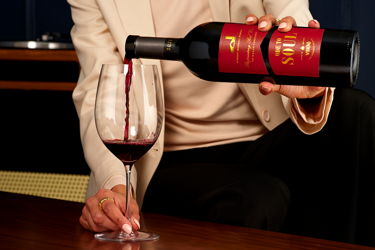 Person pouring red wine from a bottle labeled 'Ode to Soul" into a glass.