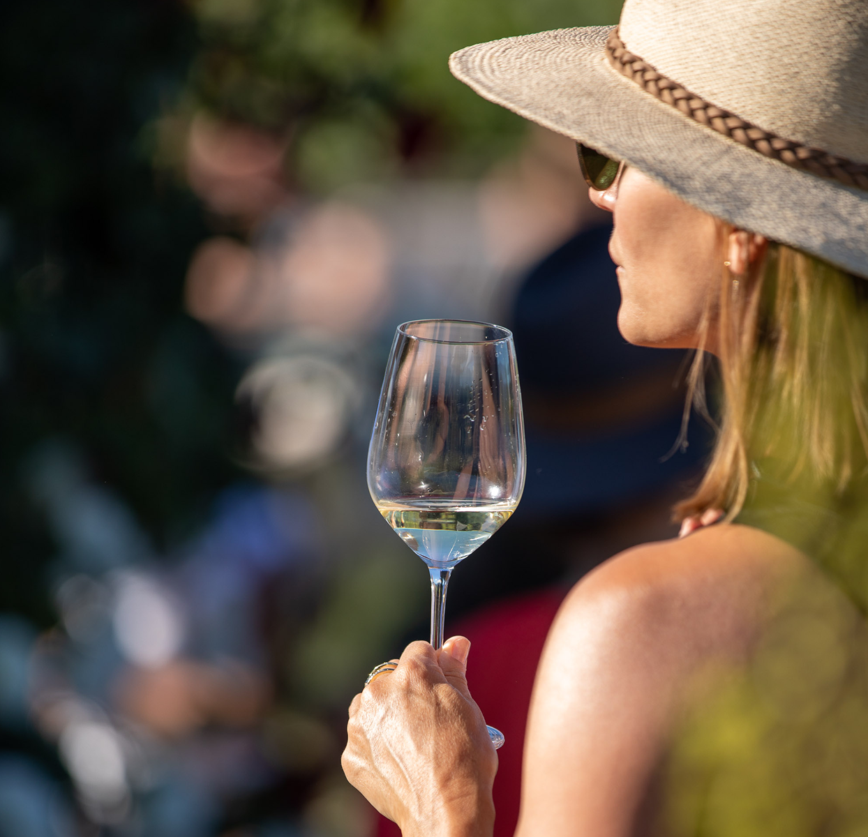 Woman wearing a hat and sunglasses drinking a glass of white wine outside 