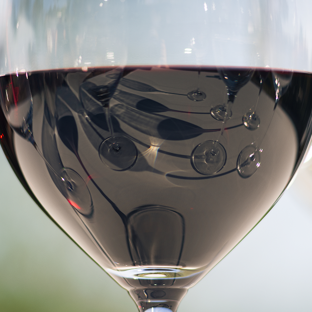 Close up image of a glass of red wine with other glasses of wine in the reflection 